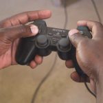 Hands holding a Sony PlayStation controller while playing a game