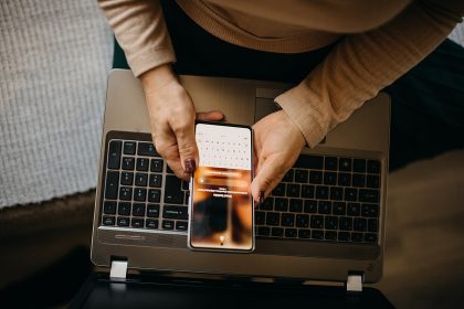Person holding a smartphone over a laptop while exploring an online platform